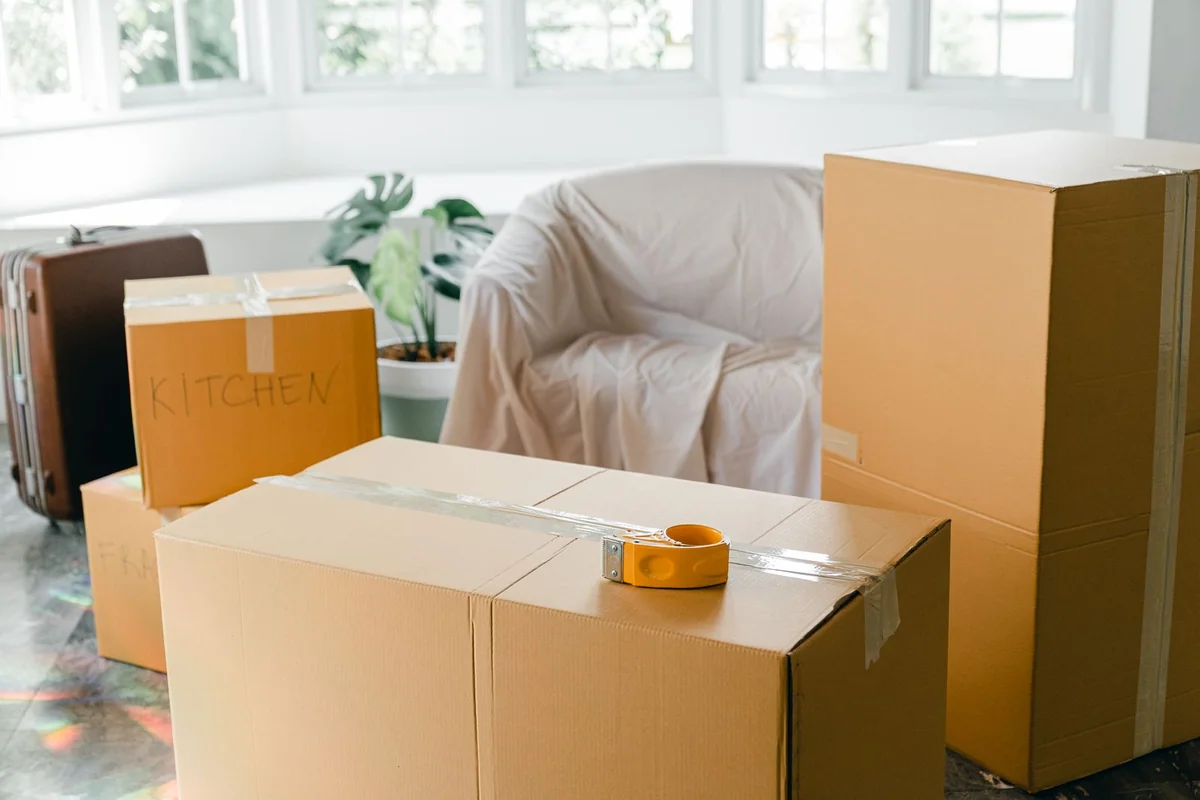 窓の明るい部屋に積まれた引越し用の段ボール箱とスーツケース